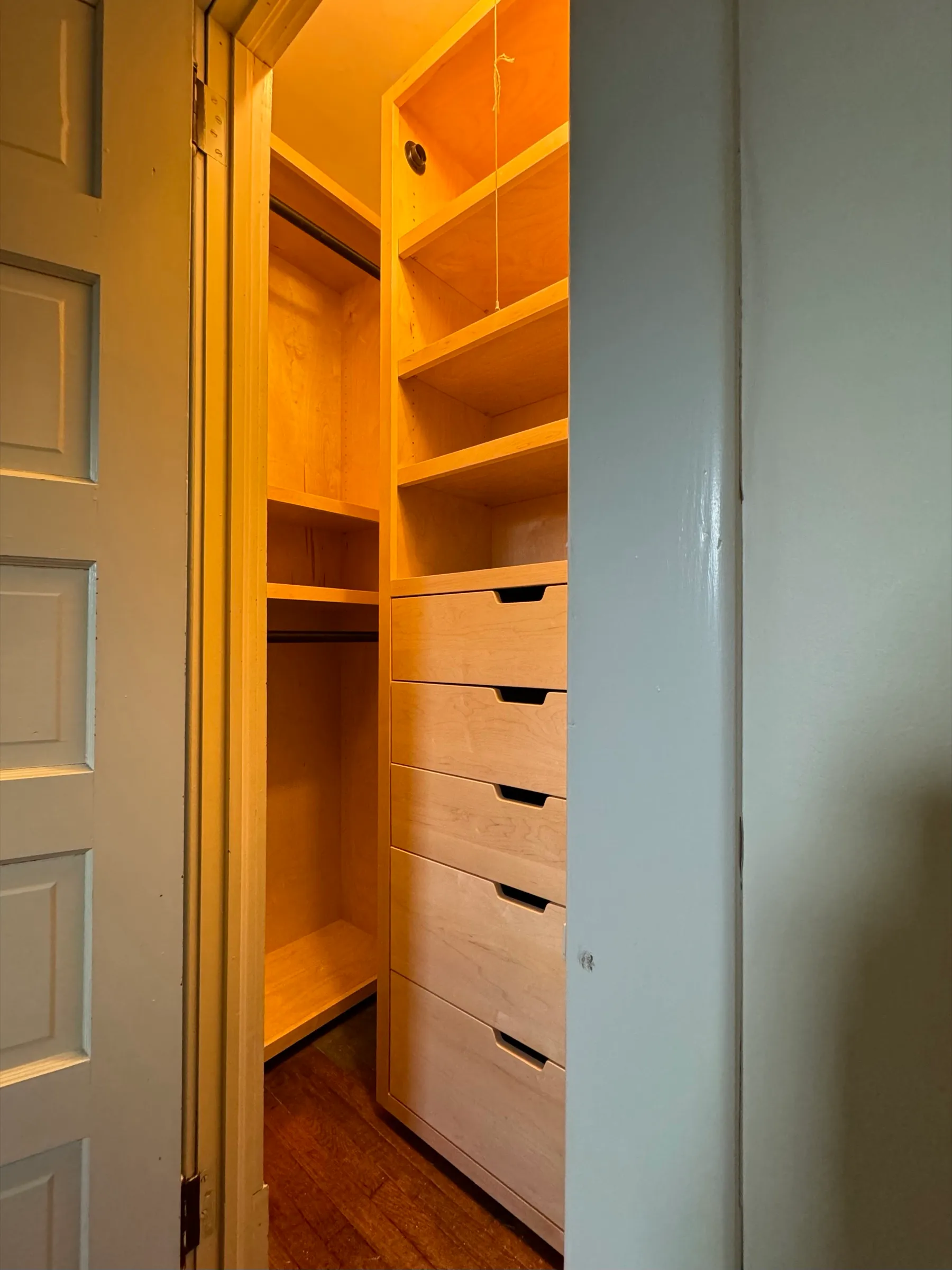 A reach-in closet seen through the doorway, with a maple shelf tower above five drawers and an open hanging section to the left.