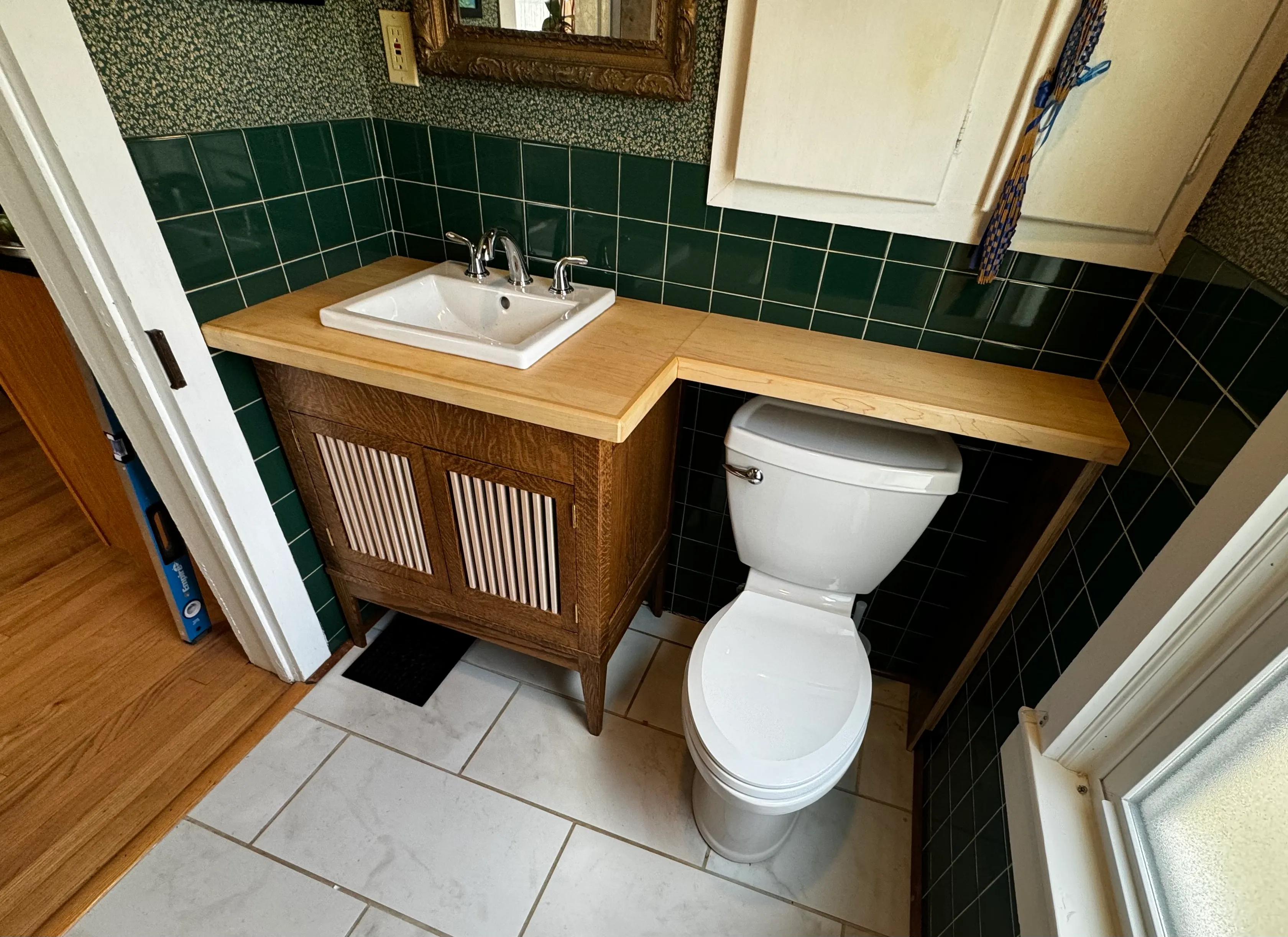 Quartersawn white oak vanity with reeded doors and a solid maple top wrapping the corner in a green-tiled bathroom, Urbana, Illinois.