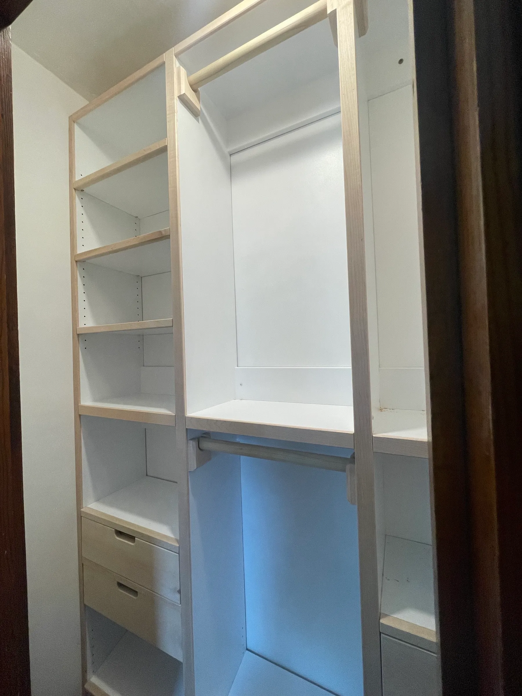 A fitted reach-in closet seen through the doorway, with maple face frames, white interiors, adjustable shelves, and a maple hanging rod.