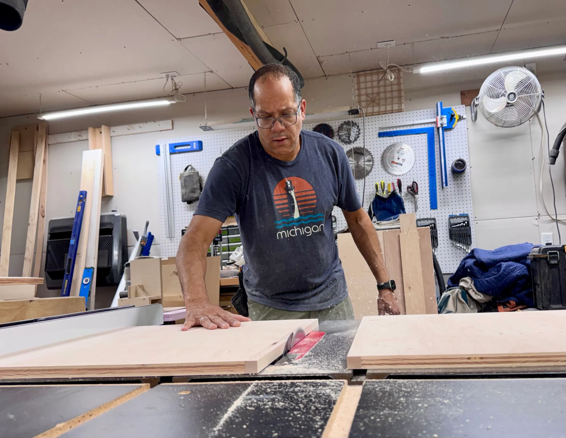 Ben Baxley guiding a maple panel through the table saw in his shop, sawdust in the air.
