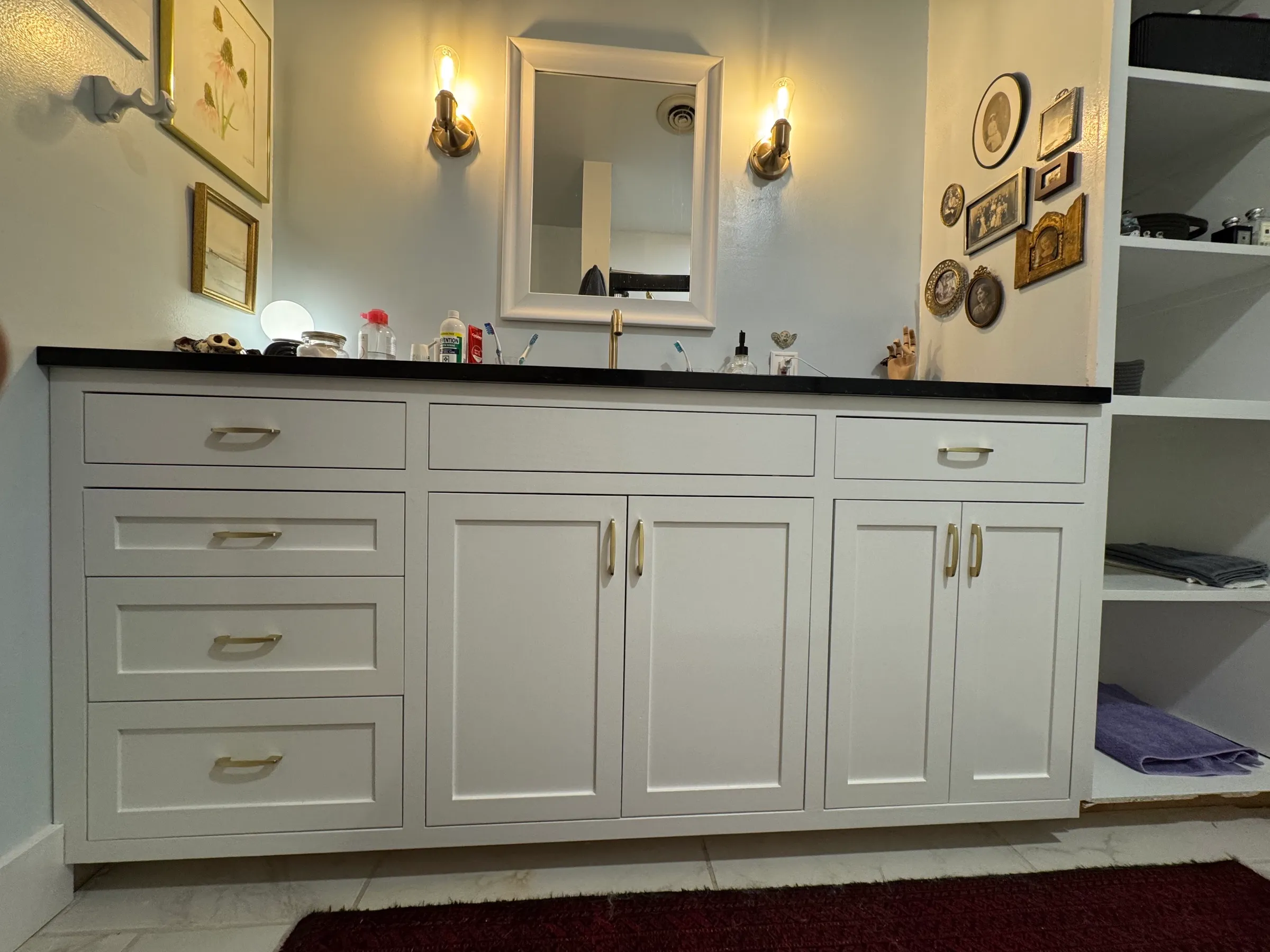 A white painted bathroom vanity with a honed black stone top and brushed brass hardware.
