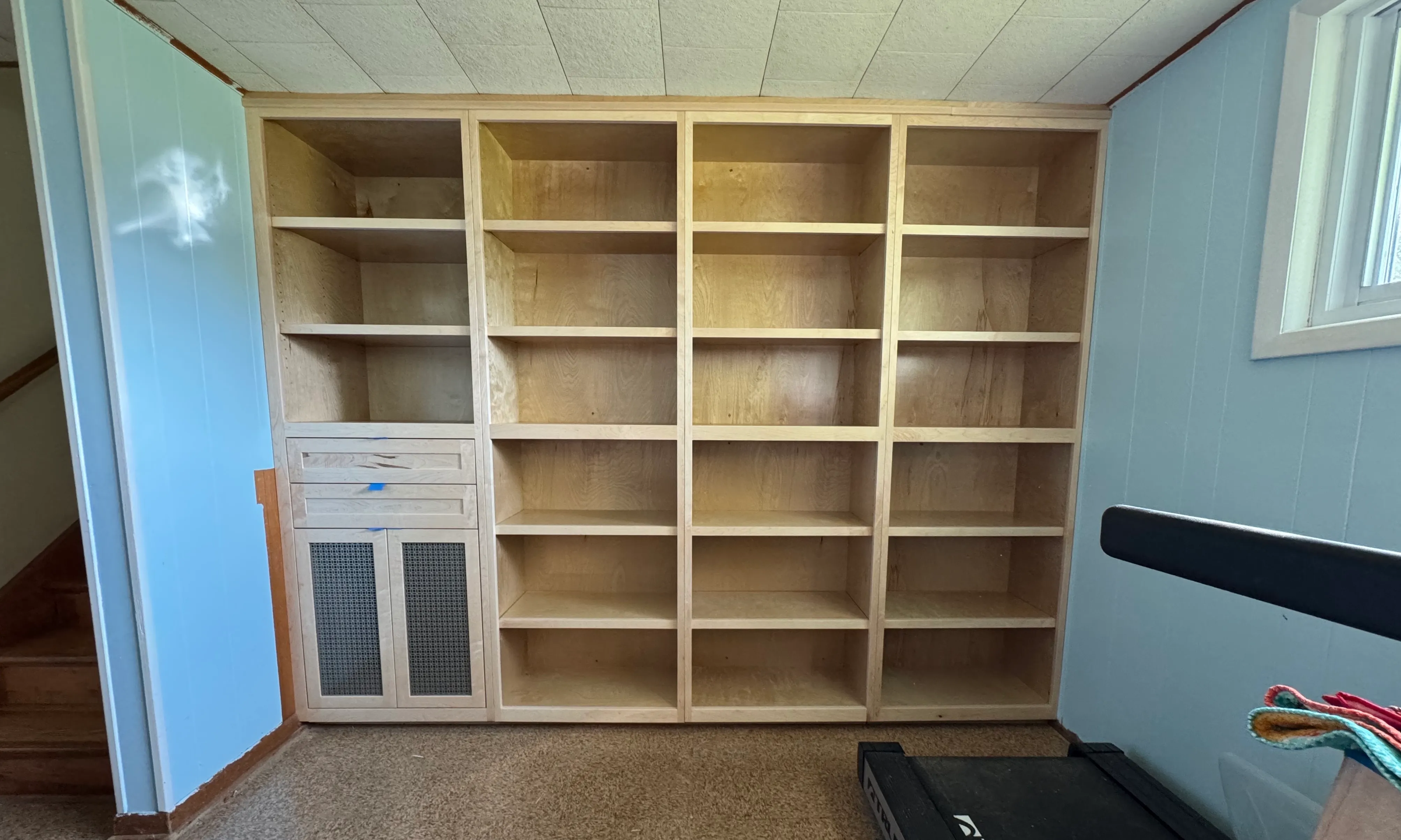Floor-to-ceiling built-in maple bookcase with open adjustable shelving and a lower cabinet with reeded doors.
