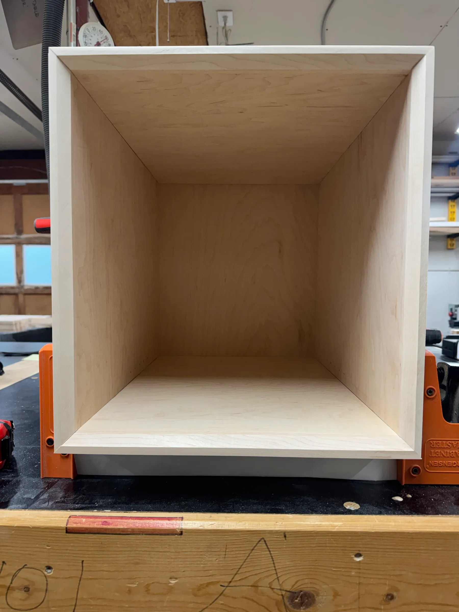 A single finished maple plywood cubby box held in a cabinet clamp on the bench, showing the clean mitered edging.
