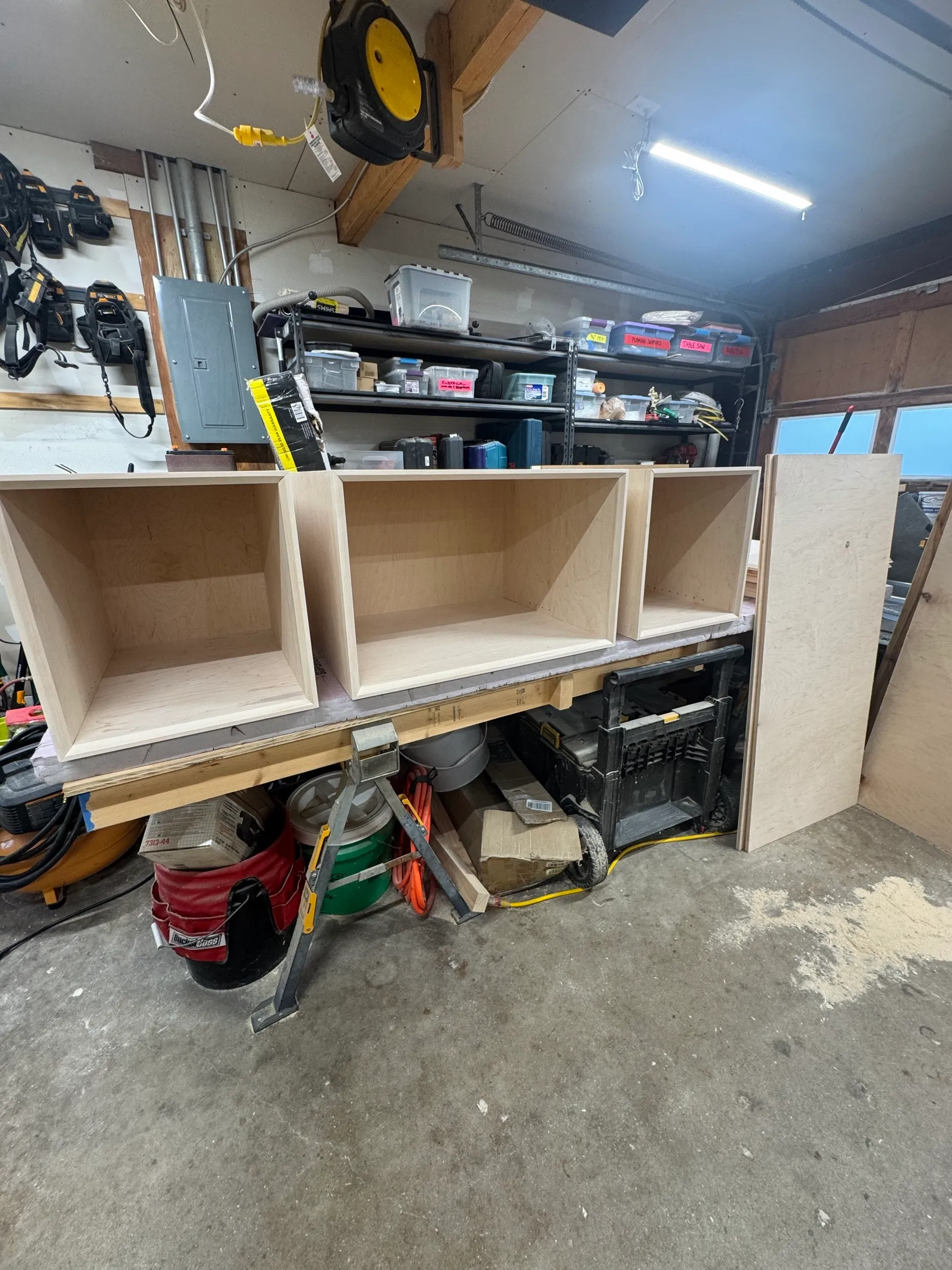 Three maple cubby boxes lined up on the shop bench, the first bay of the shelving system taking shape.