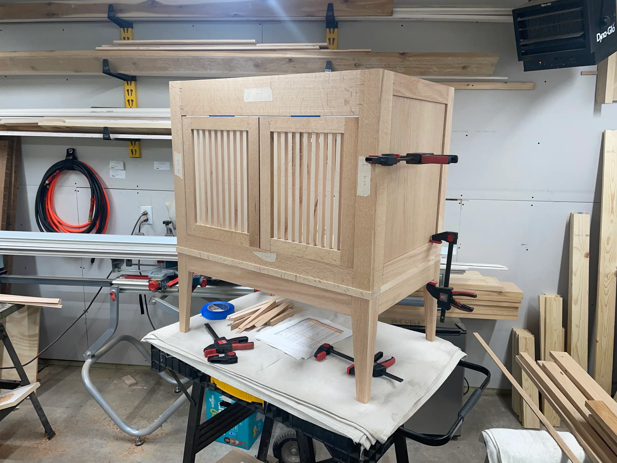 Unfinished white oak vanity carcass clamped up in the shop, reeded slat doors fitted, on a workbench.