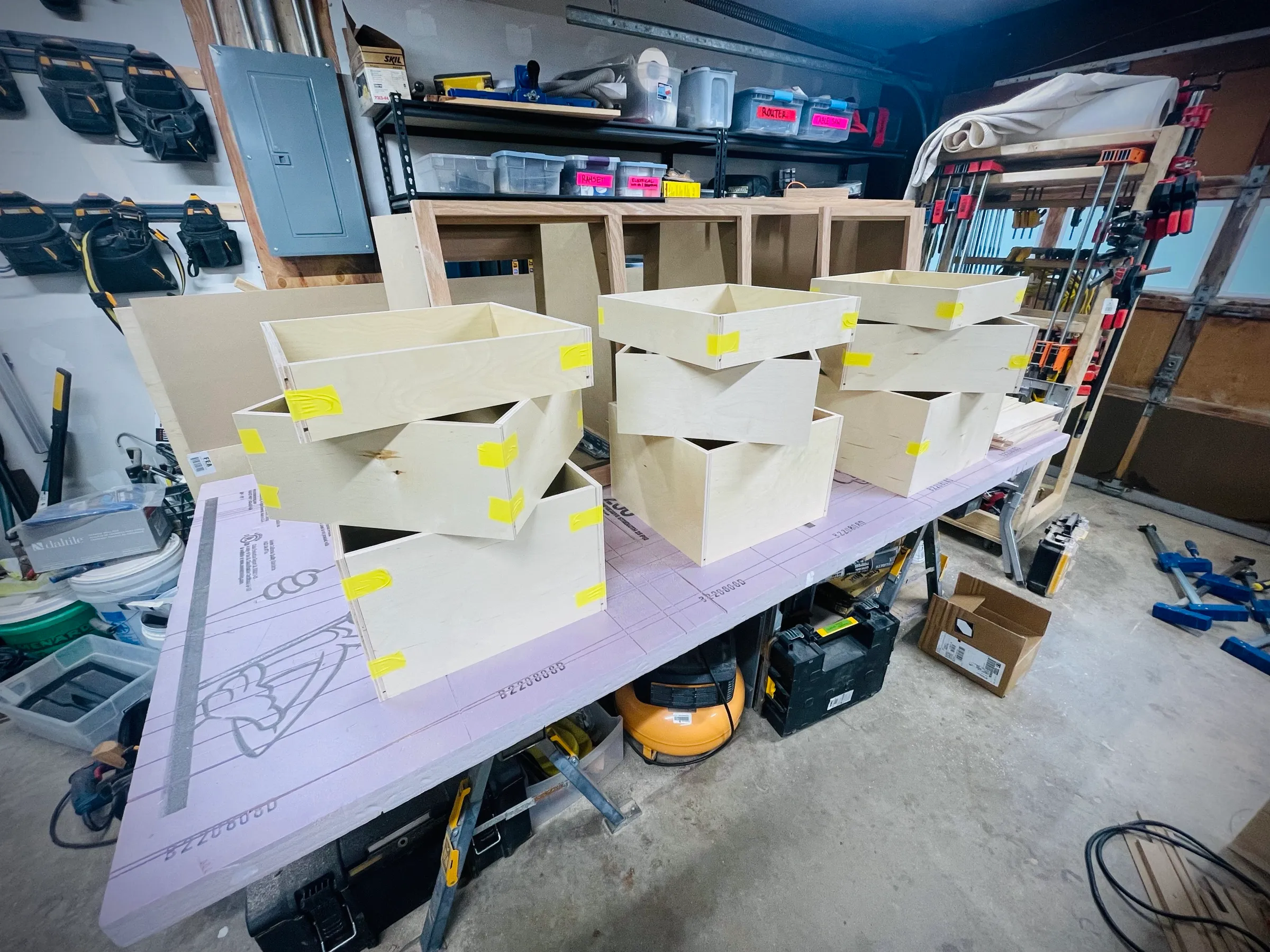 Birch plywood drawer boxes taped and stacked on the workbench during assembly.