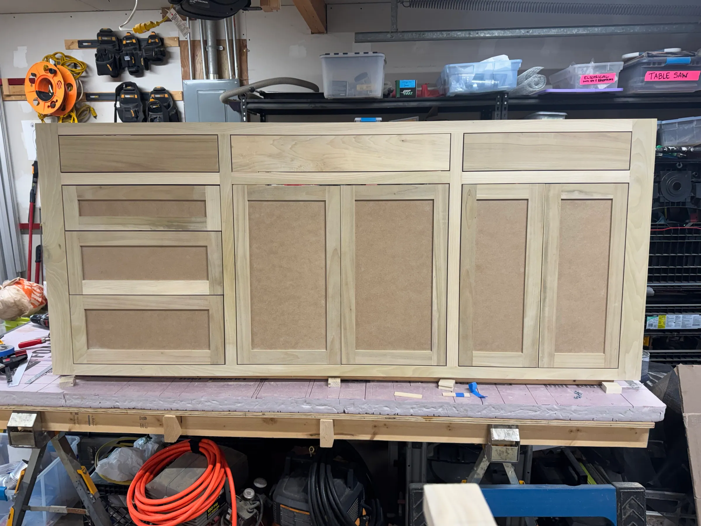 The assembled face frame standing on the bench, unfinished, with shaker drawer fronts and door panels dry-fit.