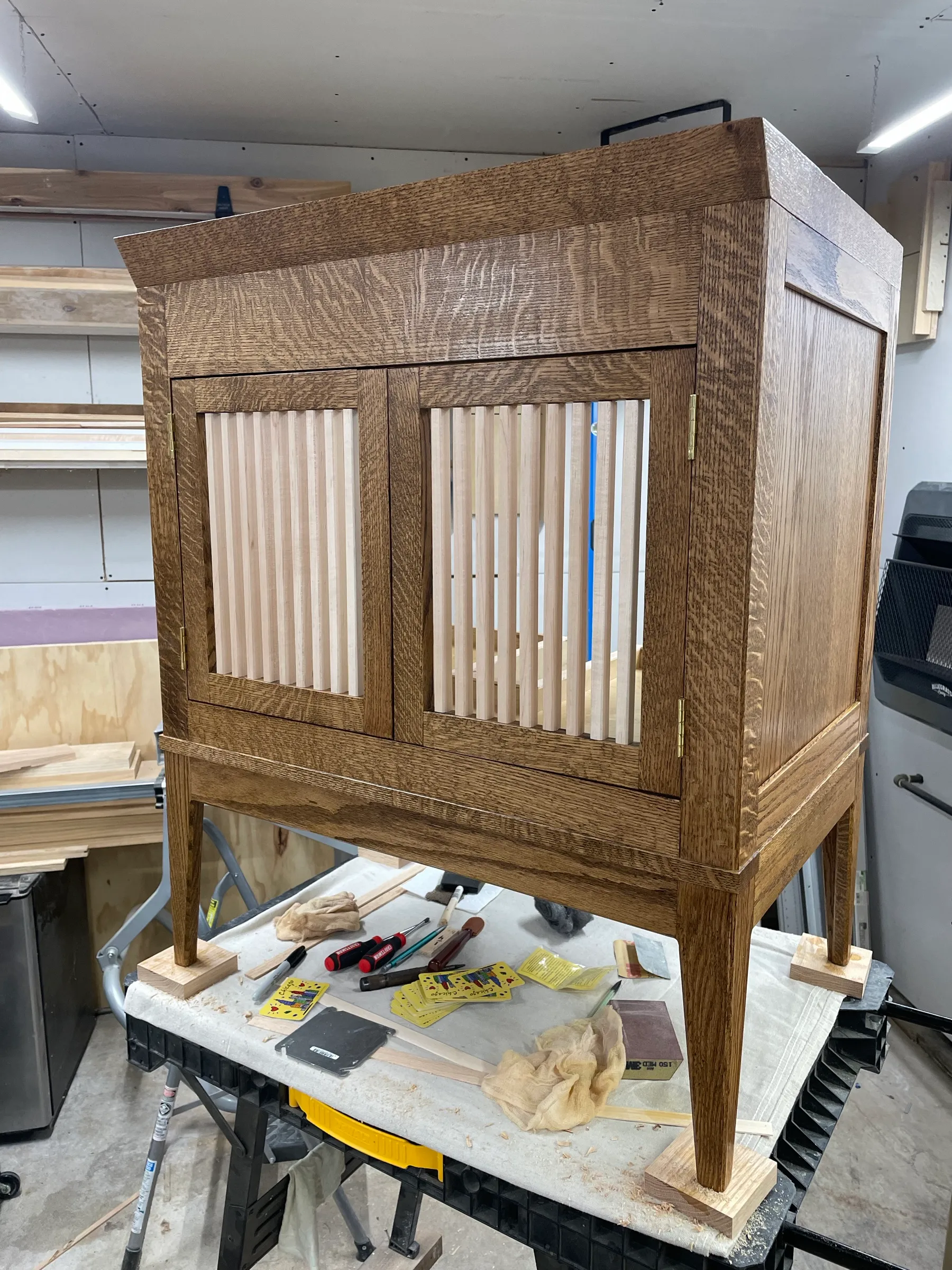 The vanity stained on the bench, showing the reeded door slats in pale maple against the darker oak and brass hinges.