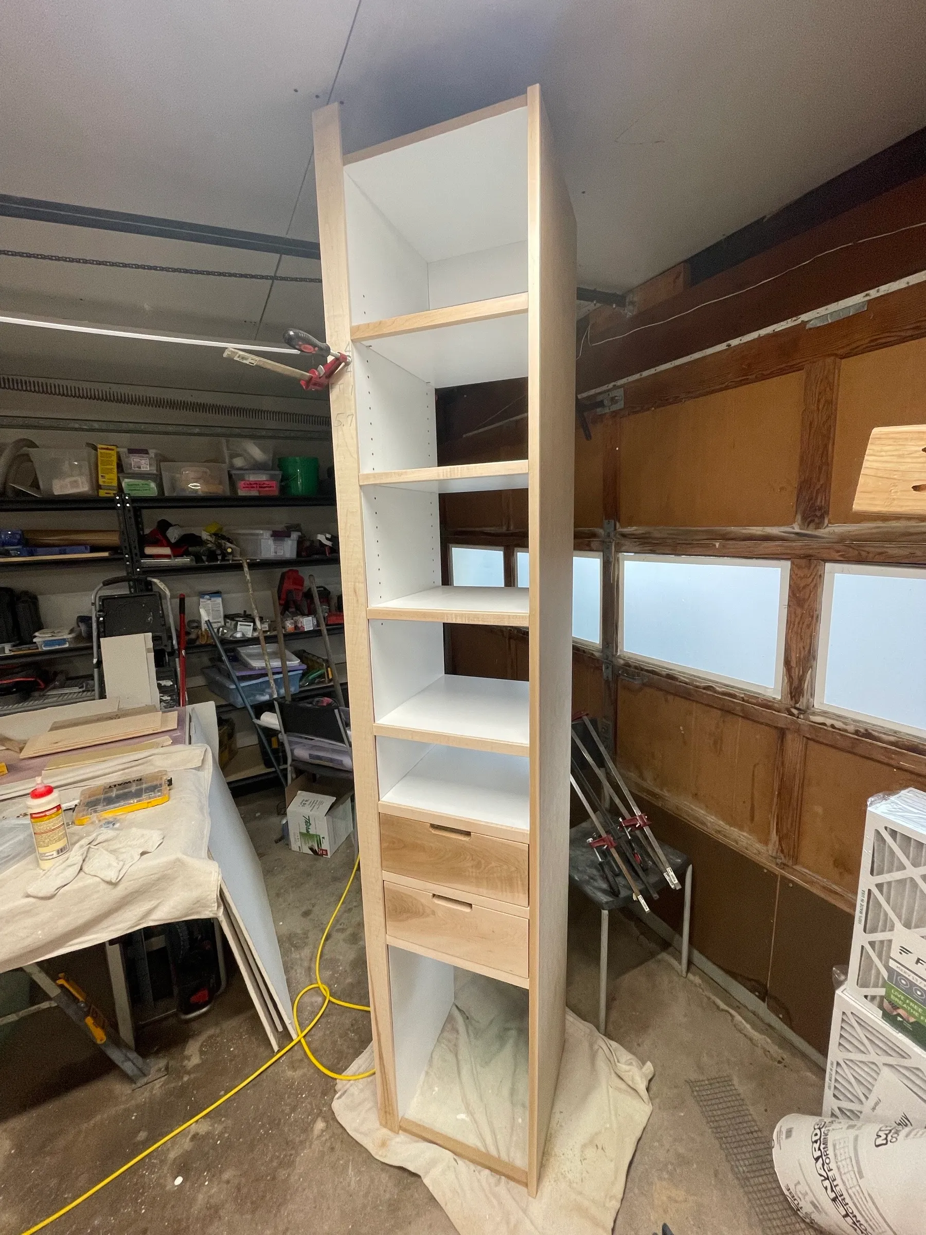The tall shelf tower standing in the shop, maple edging over white interiors with two maple drawers near the base.