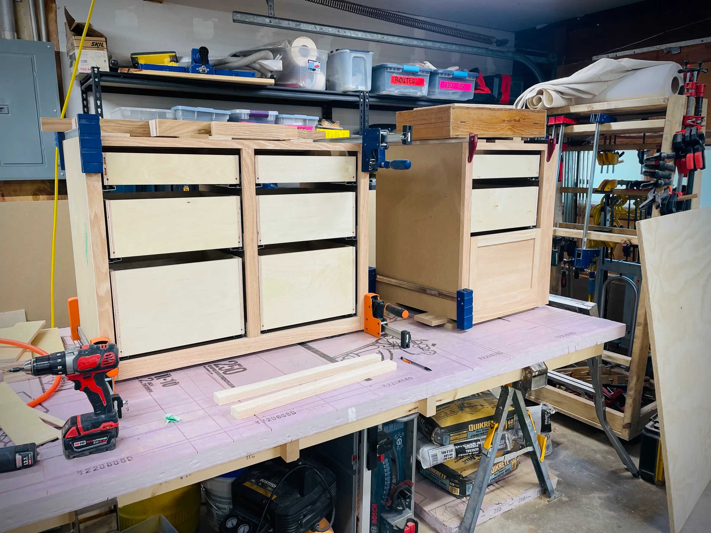 Drawer boxes clamped into a plywood cabinet carcass on the bench, drawer slides fitted.