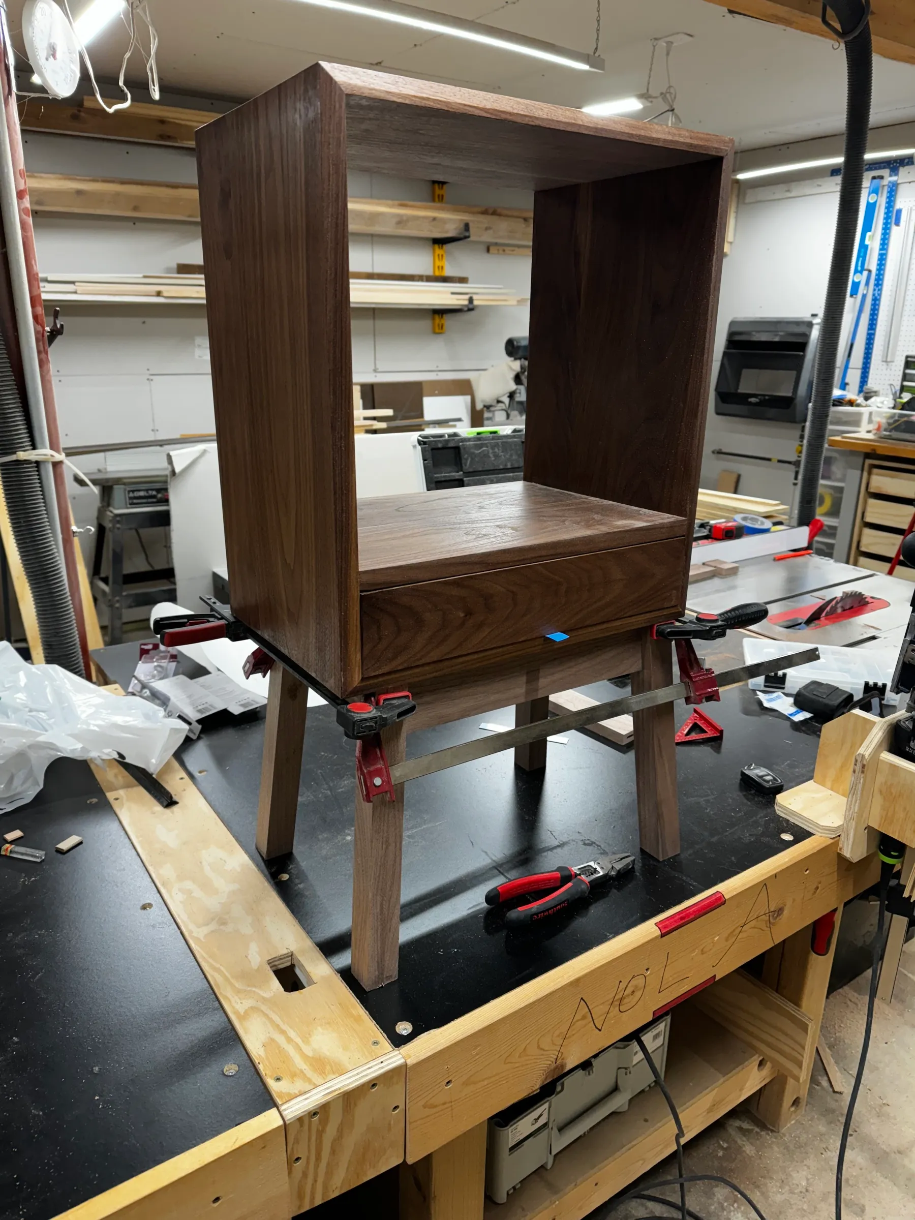 The walnut table carcass clamped up during glue-up, showing the cubby above and the angled legs.
