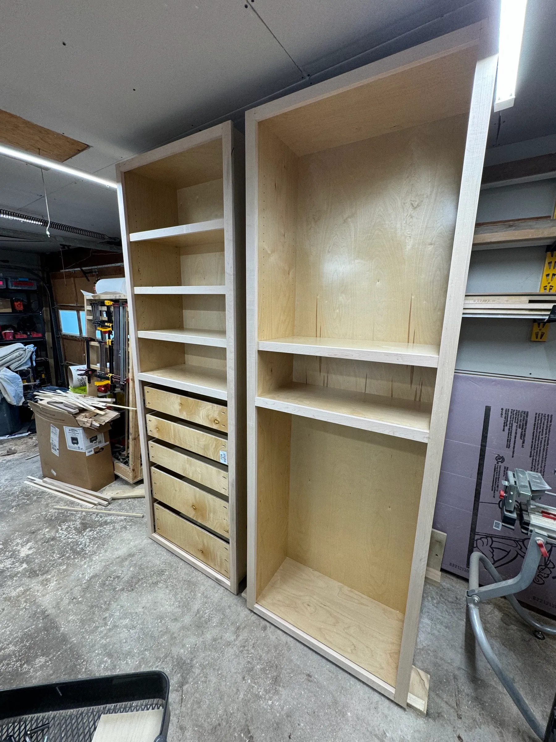 The two finished cabinet boxes standing side by side on the shop floor, one with drawers fitted and one left open for hanging.