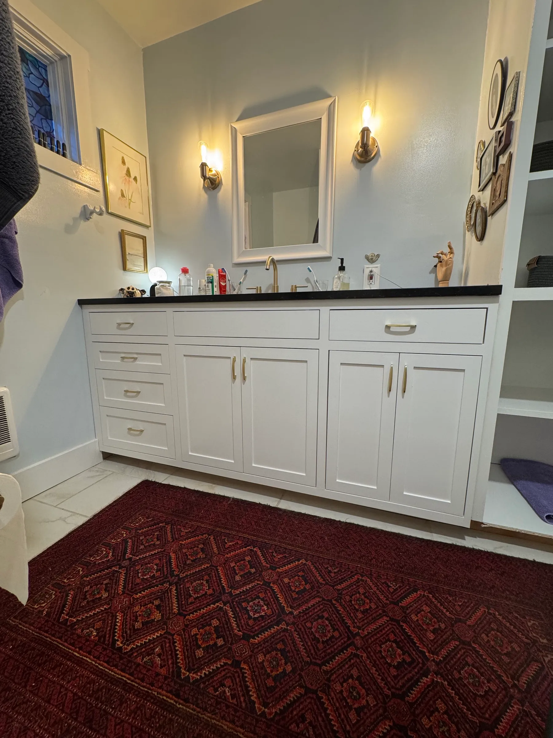 The finished white painted vanity installed wall-to-wall in the alcove with brushed brass pulls.
