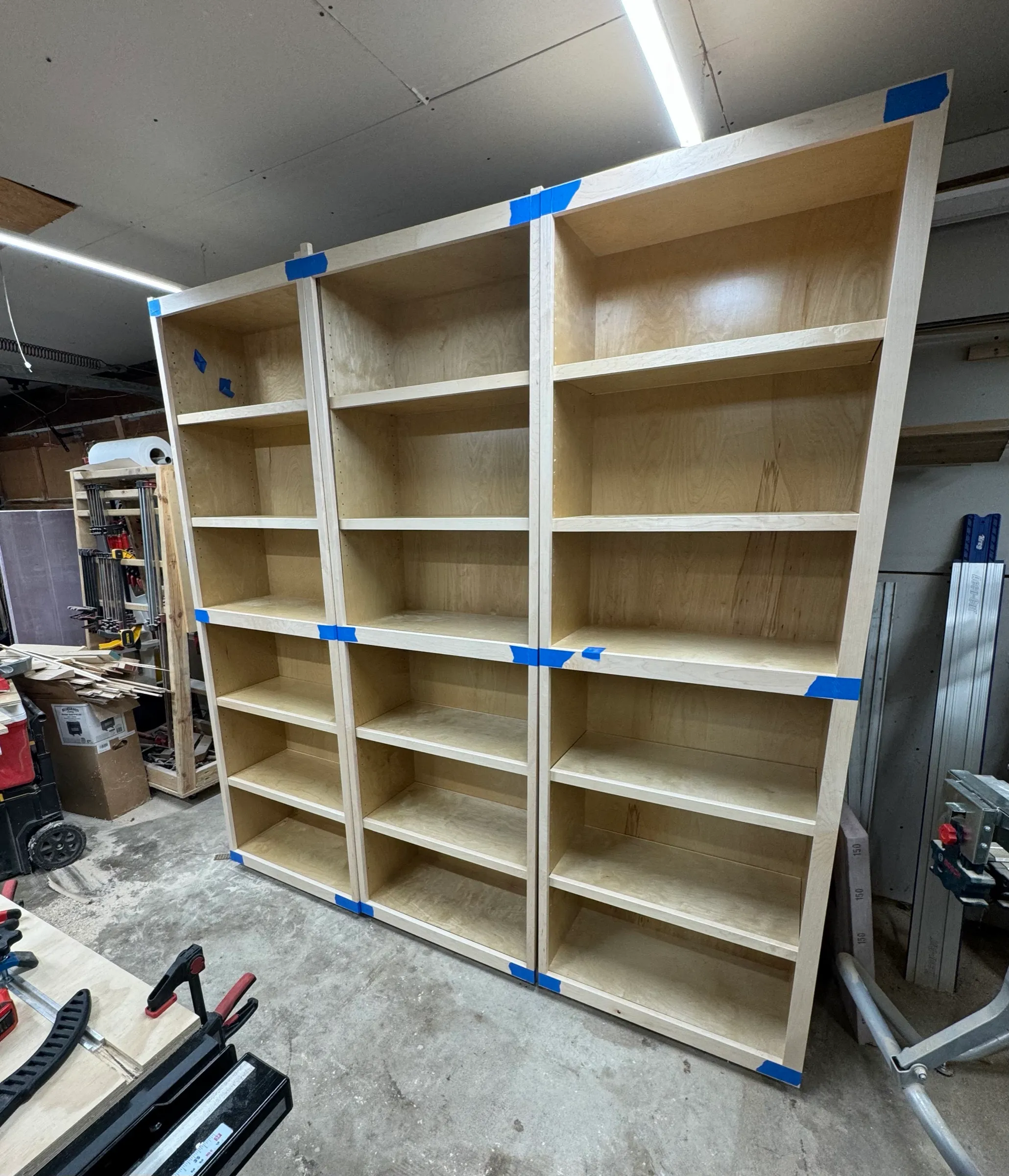 Three tall plywood bookcase carcasses standing upright and taped, rows of empty adjustable shelves.
