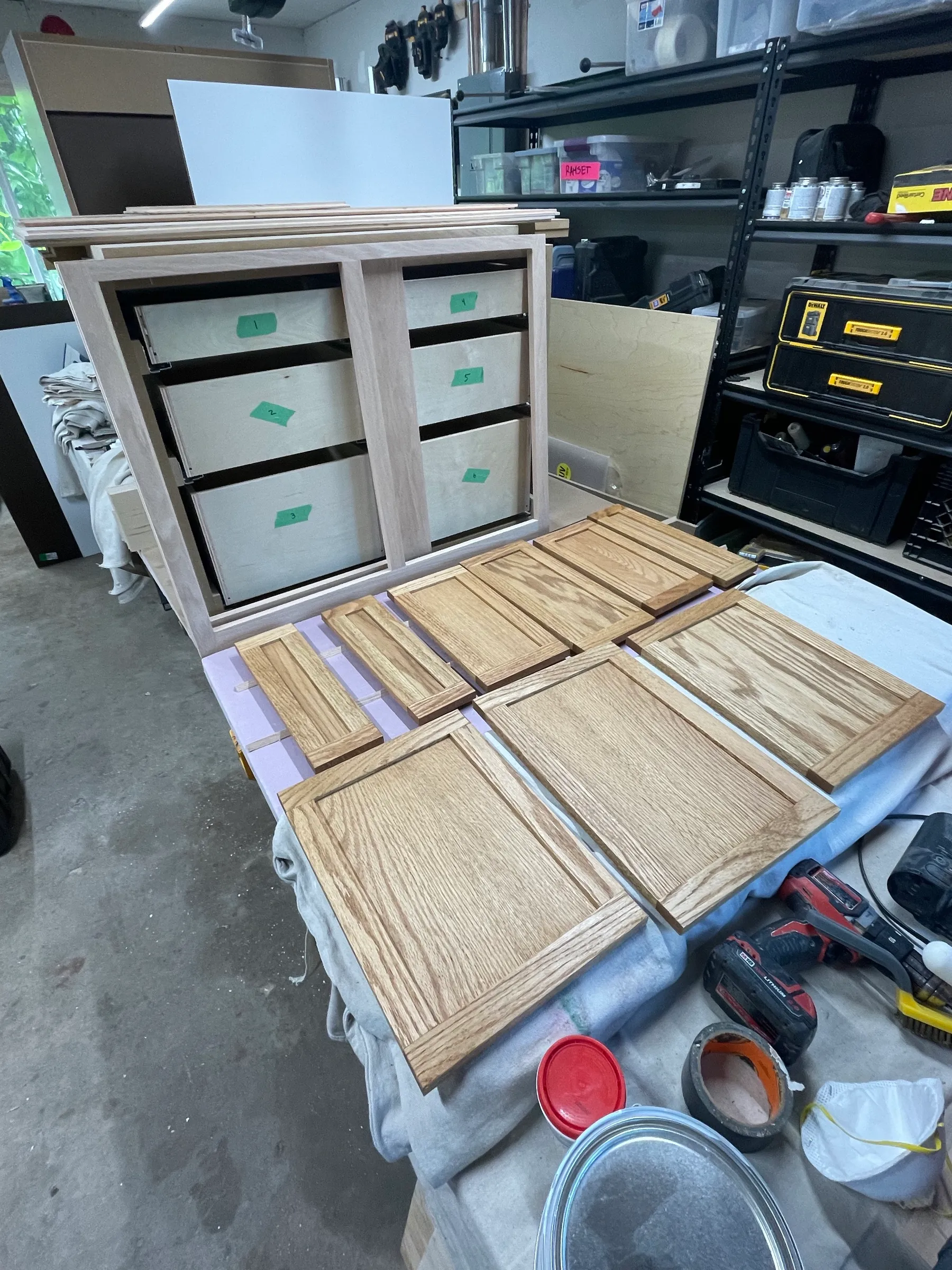 Stained red oak drawer fronts laid out to dry on a drop cloth with the plywood cabinet boxes behind.