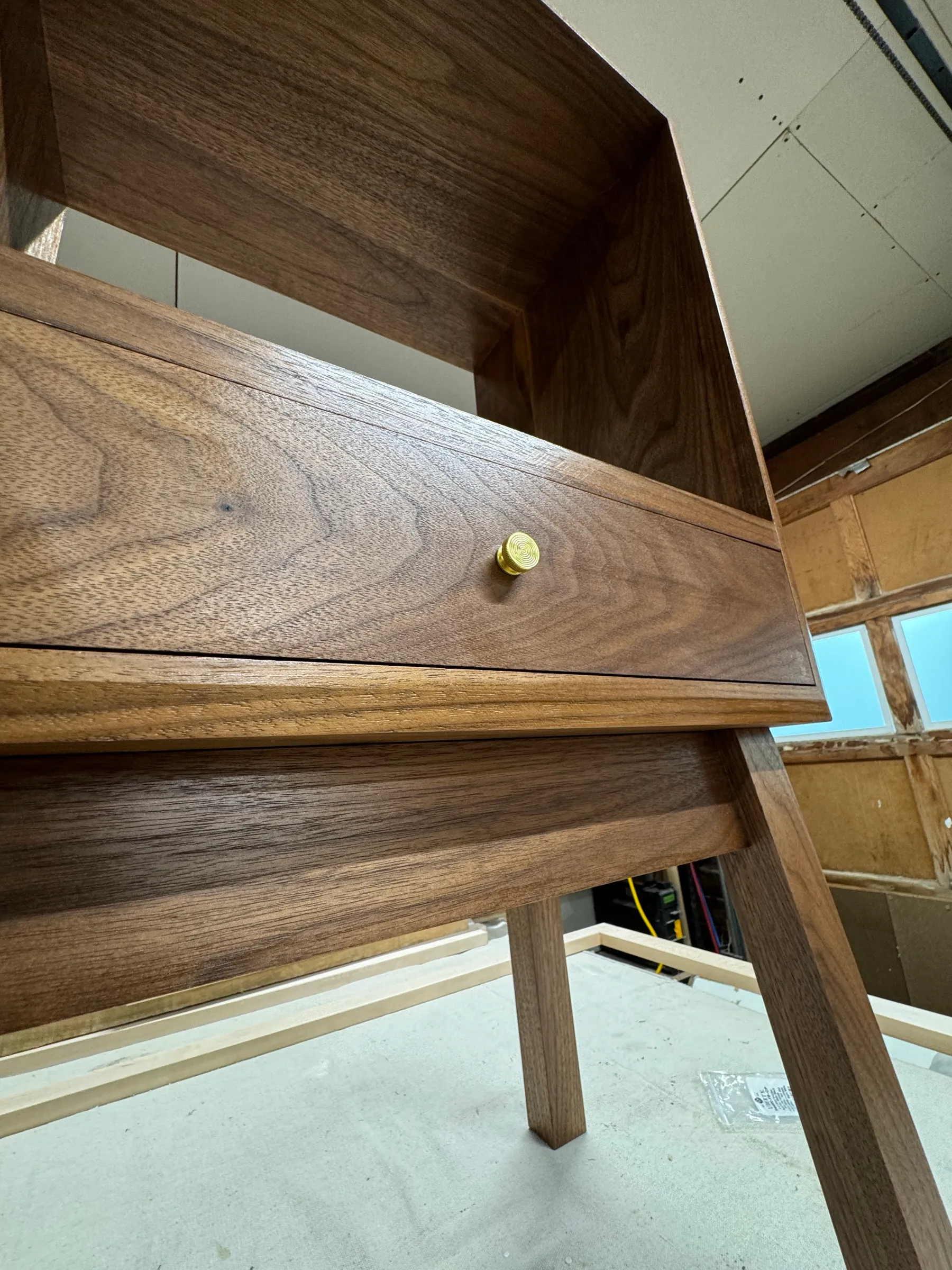 Close view of the finished walnut table with the small brass knob on the drawer and the angled leg detail.