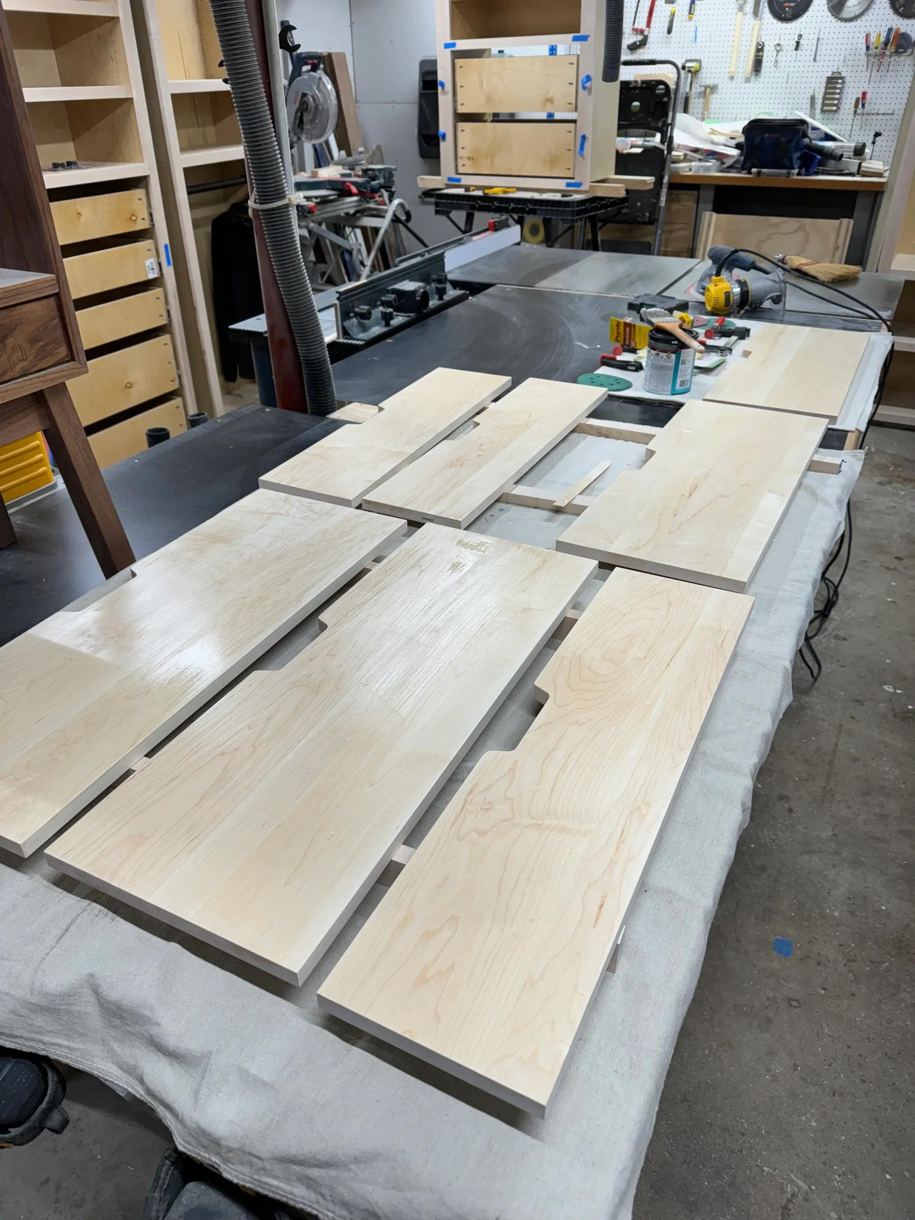 Maple drawer fronts laid out across the bench on a drop cloth, finger pulls already routed into the top edges.