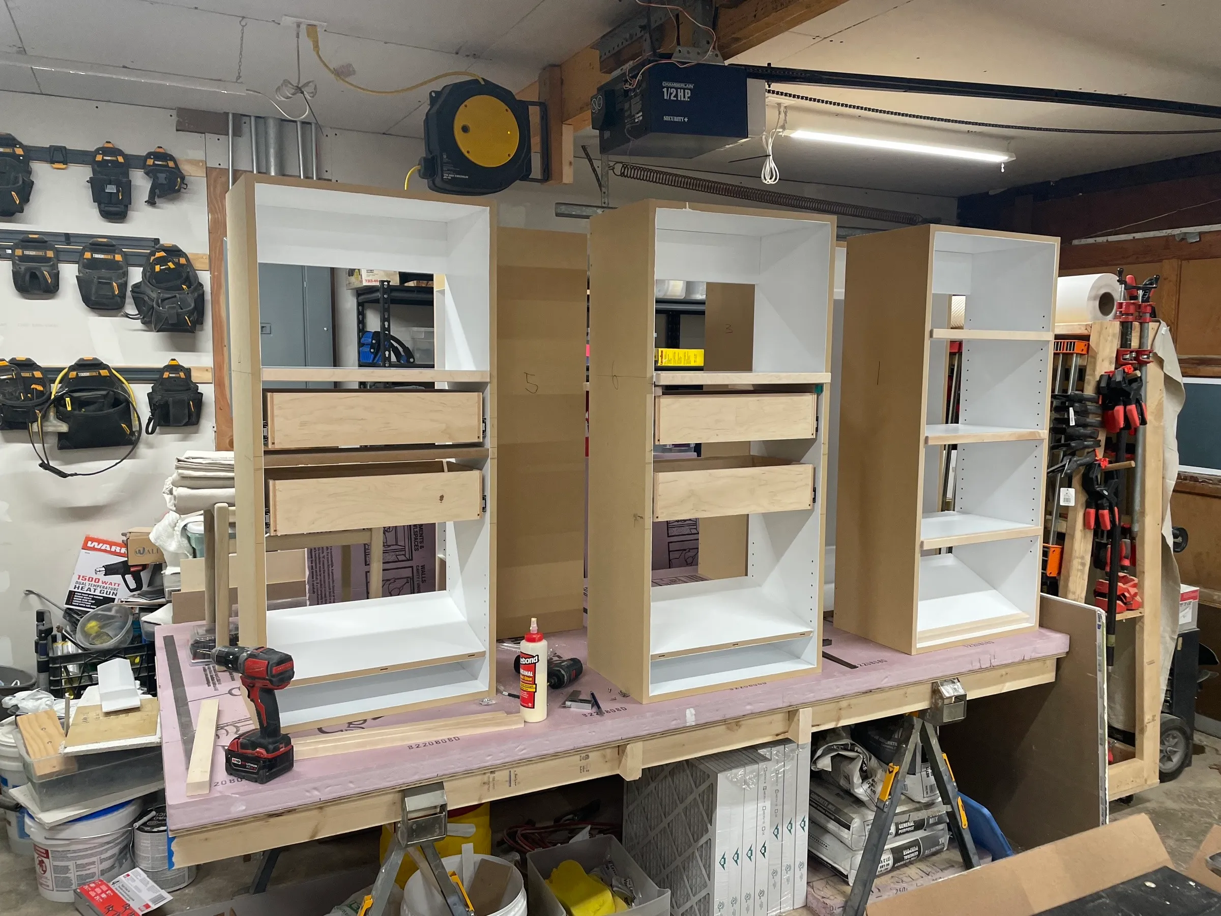 Three cabinet boxes on the bench with maple drawer boxes fitted, a drill and bottle of glue alongside.