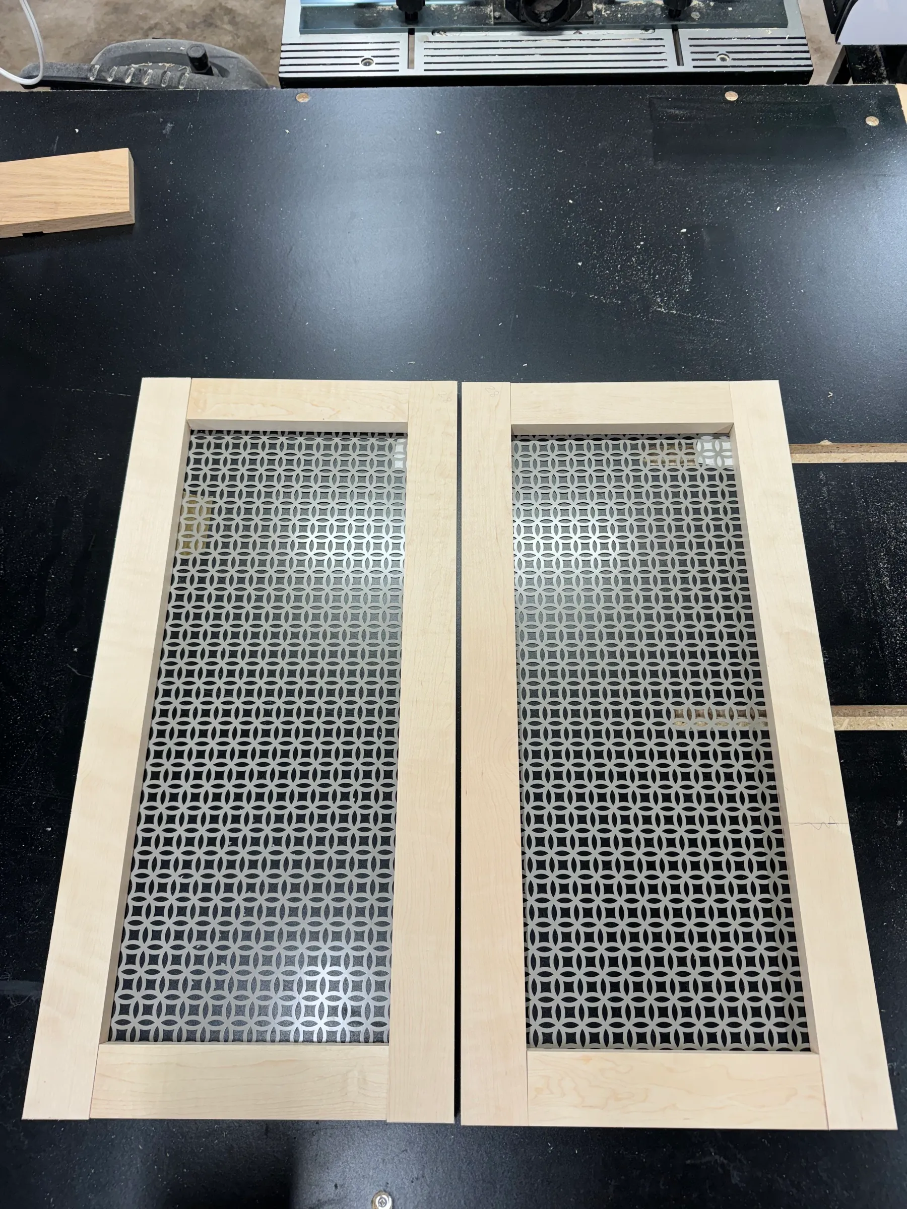 Two maple door frames with decorative perforated-metal grille panels laid out on a workbench.