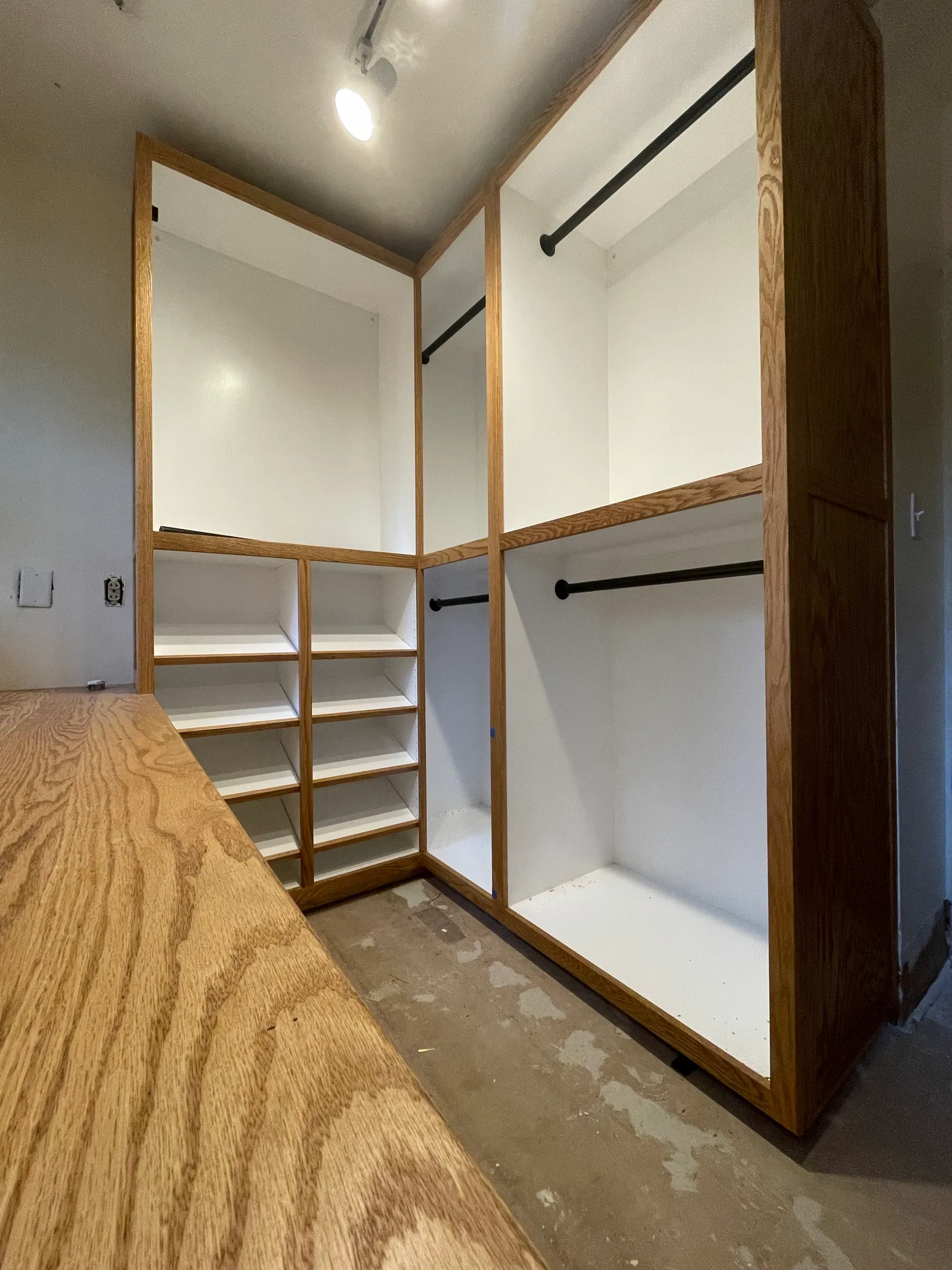 The fitted closet taking shape, oak face frames over white interiors with blackened steel hanging rods and open cubbies.
