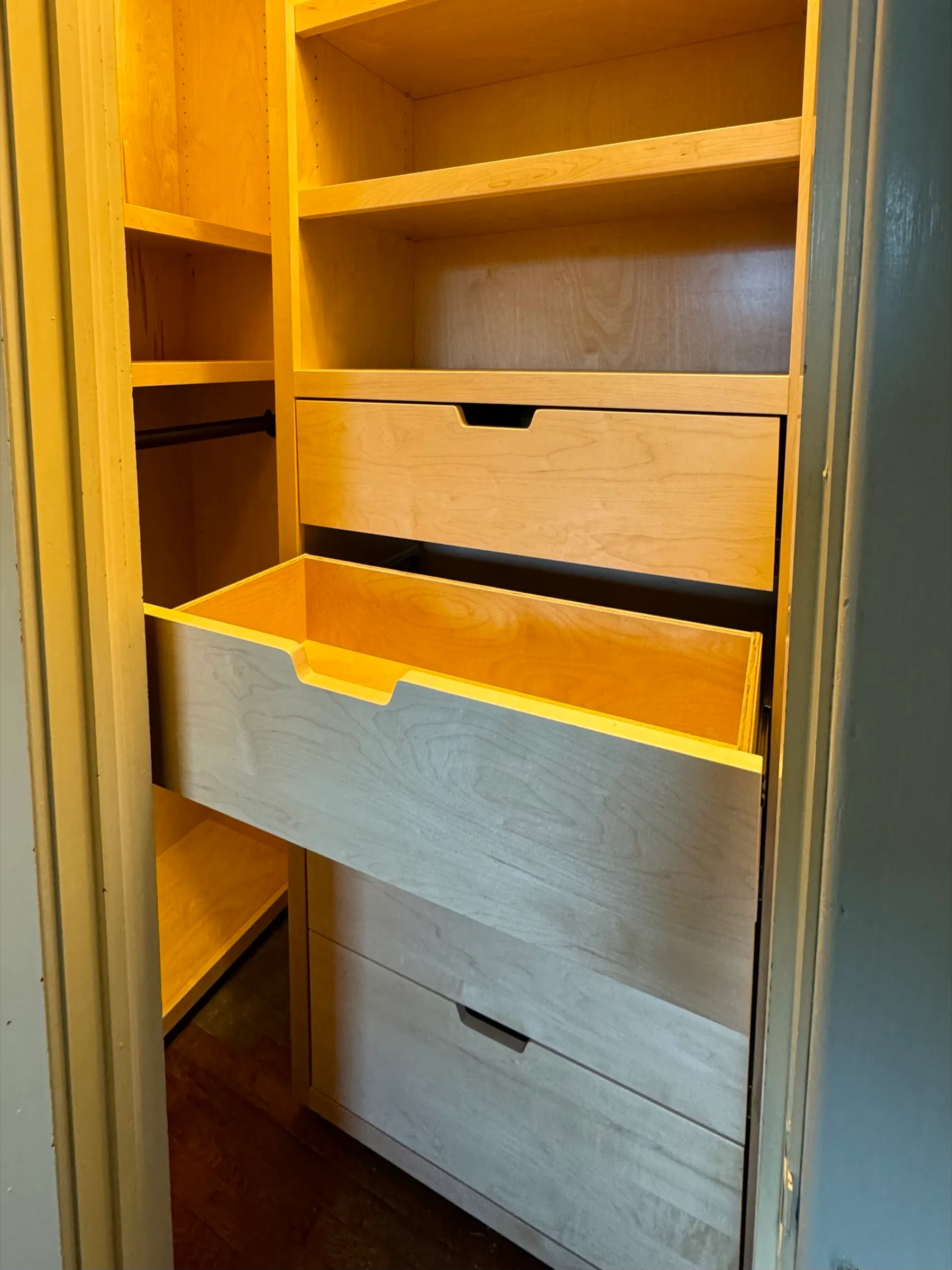 A drawer pulled open in the installed closet, showing the maple drawer box and the routed finger pull in its front.