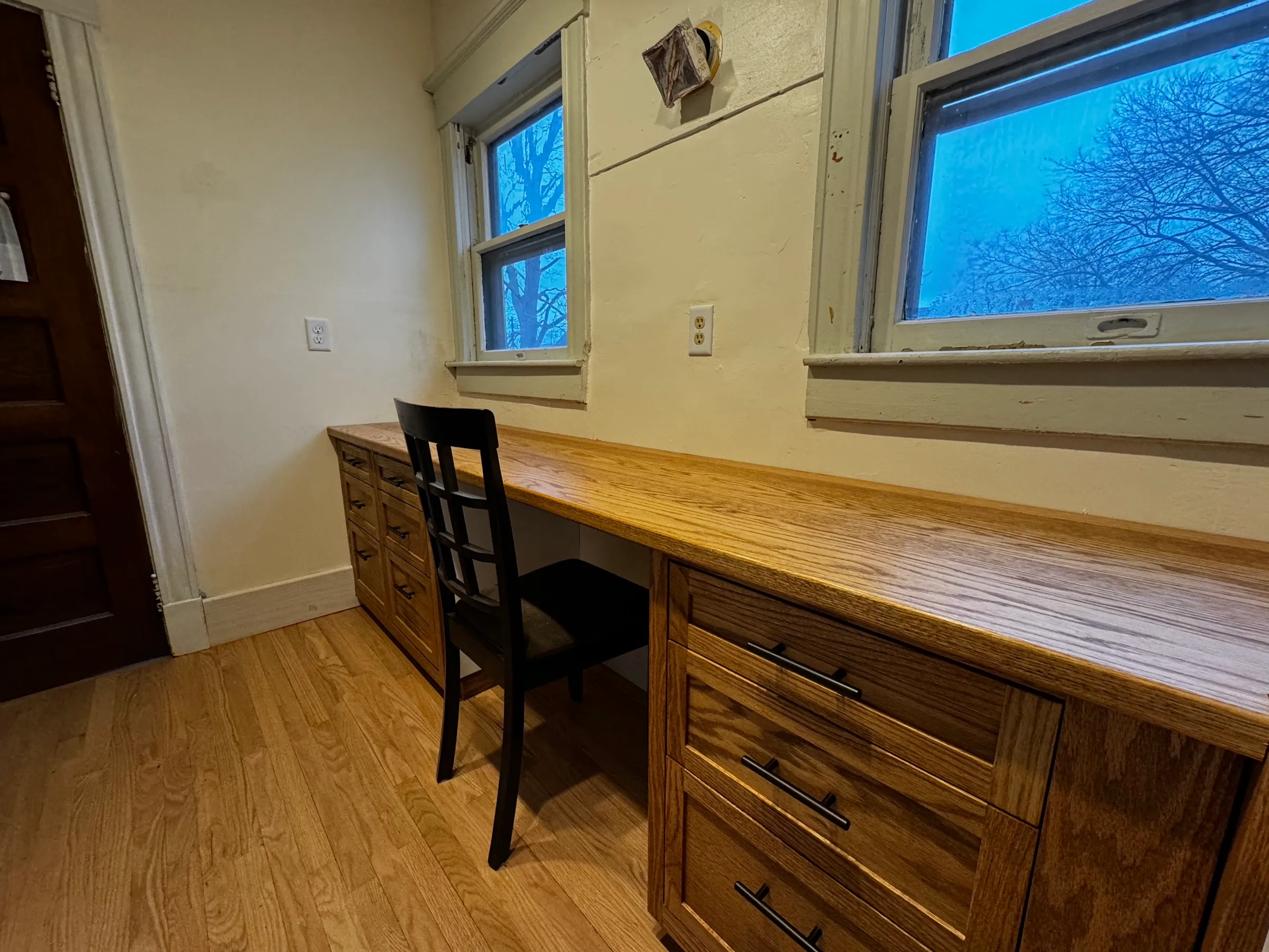 The finished walk-in with stained red oak cabinetry and drawers with black bar pulls, lit by the room windows.